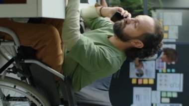 Tekerlekli sandalyedeki işadamının cep telefonuyla konuşması ve ofiste çalışırken konuşma sırasında not alması.