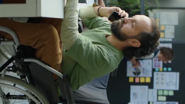 坐在轮椅上的商人在办公室工作时用手机交谈和记笔记的垂直镜头 — 图库视频影像