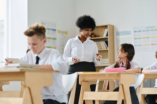 Young teacher talking to schoolgirl during lesson at school