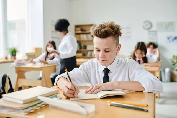 Uczeń Robi Notatki Notatniku Siedząc Przy Biurku Podczas Lekcji — Zdjęcie stockowe