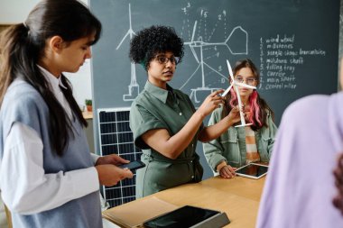 Öğretmen derste bir grup öğrenciye yel değirmeninin çalışmalarını anlatıyor.