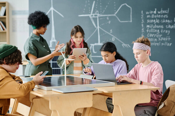 Group of students using gadgets to learn new technology with teacher during lesson in the classroom