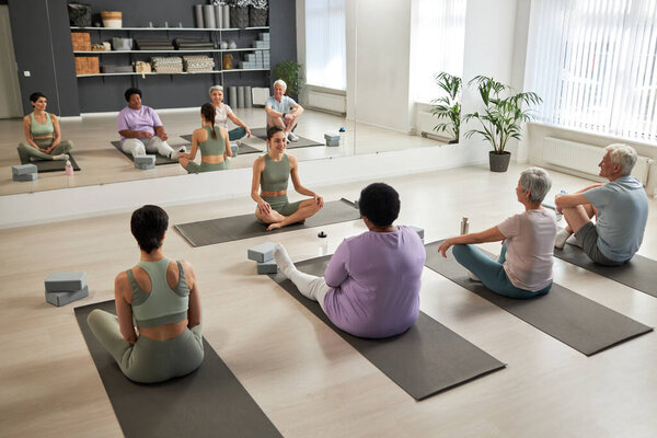 High angle view of group of people exercising together with instructor in yoga studio