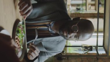 Afro-Amerikalı iş adamının öğle yemeği yerken ve kafede iş arkadaşlarıyla konuşurken dikey görüntüsü.