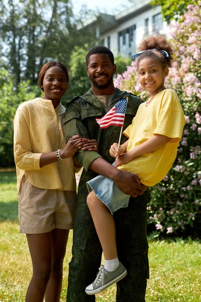 Vertical image of African American happy family with child and military dad smiling at camera outdoors
