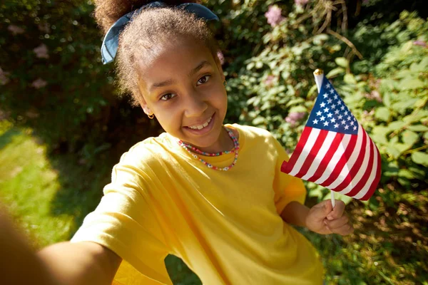 Portrait of African American girl with american flag smiling at camera outdoors
