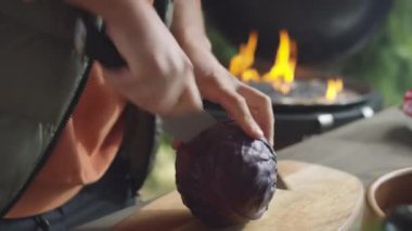 Tahtaya saplanmış bıçakla kırmızı lahana kesen bir adamın elleri.