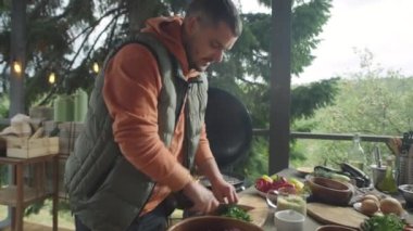 Yemek blogcusu kasede salataya maydanoz ekliyor ve dışarıda barbekü terasında ana yemek dersi verirken kamerada konuşuyor.