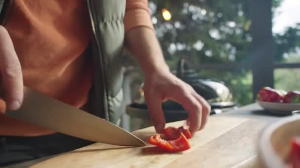 屋外で食べ物を調理しながら赤いベルペッパーを切った男性シェフの手のクローズアップショット — ストック動画