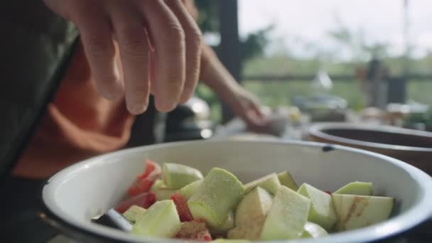 屋外テラスで食べ物を準備しながらボウルに野菜ミックスにスパイスと塩を追加する男性シェフの手の近くショット — ストック動画