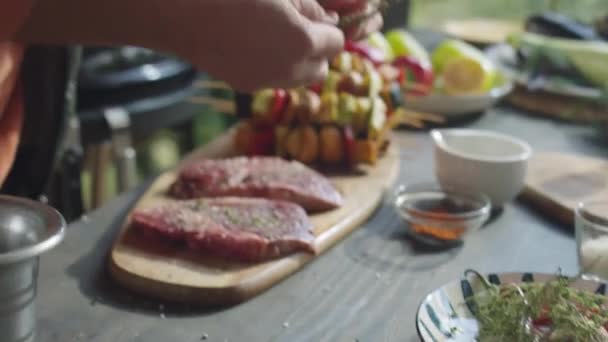 屋外テラスでそれらを焼く準備しながら生の肉ステーキに芳香族のハーブを加える男性シェフの手のクロップショット — ストック動画
