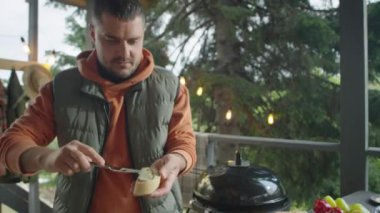 Erkek yemek blogcusunun, açık terasta bbq bruschetas pişirirken ızgara ekmek dilimlerinin üzerine yayıldığı ve kamera önünde konuştuğu görüntüleri.