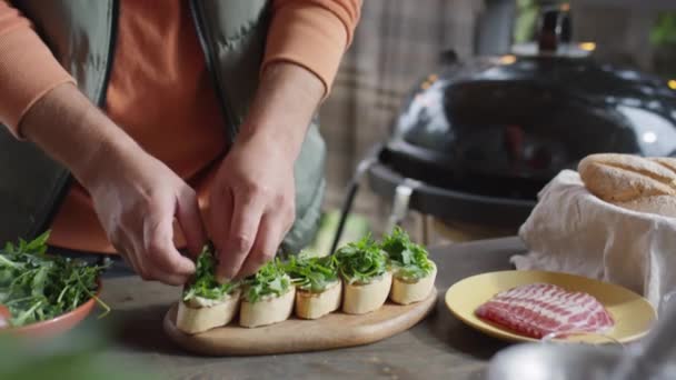 屋外テラスでブルシェッタスを調理しながら 新鮮なアルグラの葉をパンに追加する男性シェフのクロップショット — ストック動画