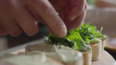 Bir adamın bruschetalara taze roka yaprağı ekleyip aperatifleri hazırlarken yakın plan çekimleri.