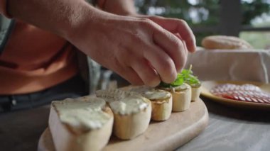 Açık terasta aperatifler pişirirken erkek şefin bruschetalara roka yaprakları eklediği yakın çekim.