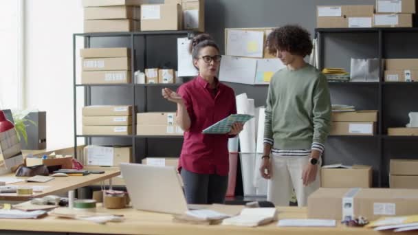 クリップボードを持っている女性マネージャーと配達サービスオフィスで勤務中の若い男性従業員にタスクを説明 — ストック動画