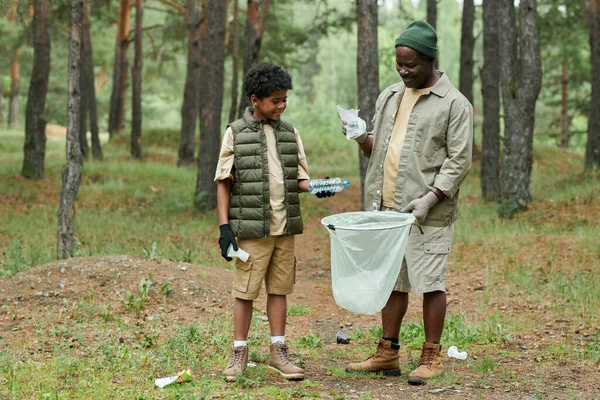 African American dad cleaning forest from garbage together with his son