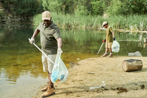 Dad cleaning the water from garbage together with his son outdoors