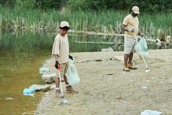 Family of two cleaning the territory of lake together outdoors