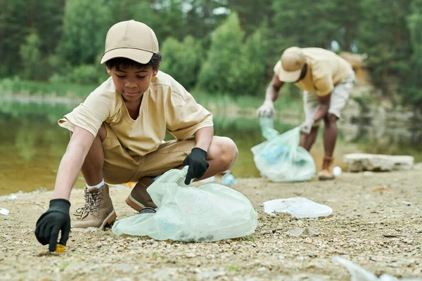 African American child cleaning territory around the lake together with his dad in background