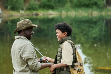 İki kişilik mutlu Afrika kökenli Amerikalı aile göl kenarında birlikte balık tutuyor.