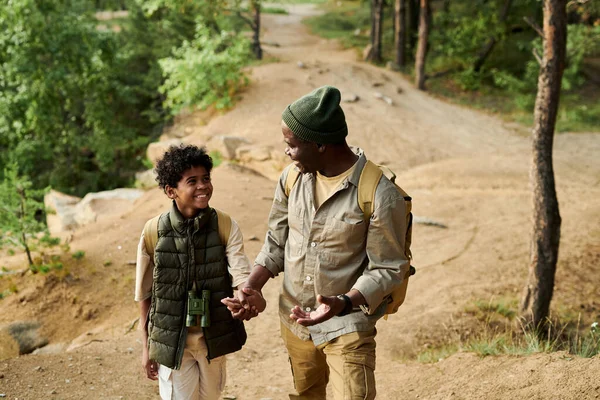 Happy African American dad travelling together with his son in the forest