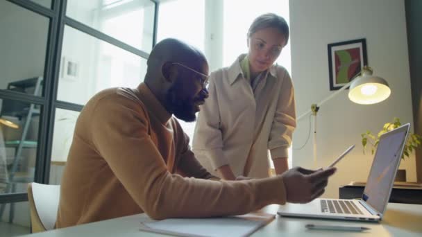 非裔美国商人坐在办公室的办公桌前 在工作日与白人女性同事讨论笔记本电脑项目 — 图库视频影像