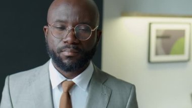 Resmi takım elbiseli ve gözlüklü Afro-Amerikan iş adamının ofisinde kameraya poz verirken çekilen göğüs fotoğrafı.