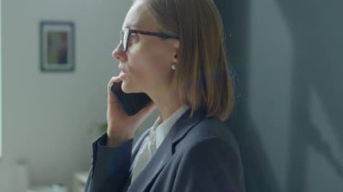 Resmi giysili ve gözlüklü sarışın iş kadınının ofiste cep telefonuyla konuşurken çekilen göğüs görüntüsü.