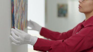 Beyaz eldivenli kadın galeri müdürünün duvara resim asıp sergiye hazırlanırken çekilmiş görüntüsü.