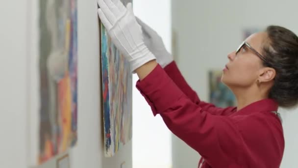 Beyaz Eldivenli Bayan Galeri Çalışanı Sergi Salonunda Çalışırken Duvardaki Resimleri — Stok video