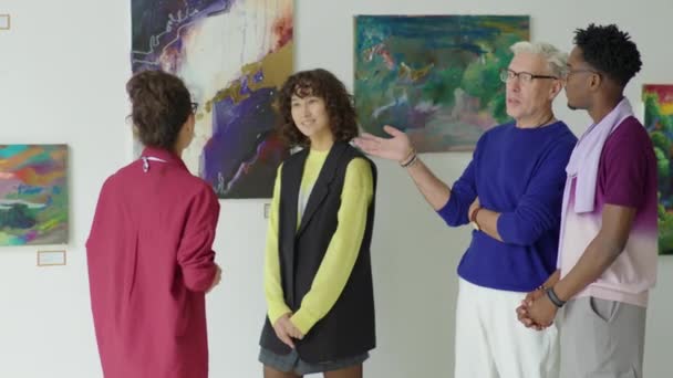 女性ギャラリーガイド 現代美術展を巡るツアーをしながら訪問者のグループに絵画について語る — ストック動画