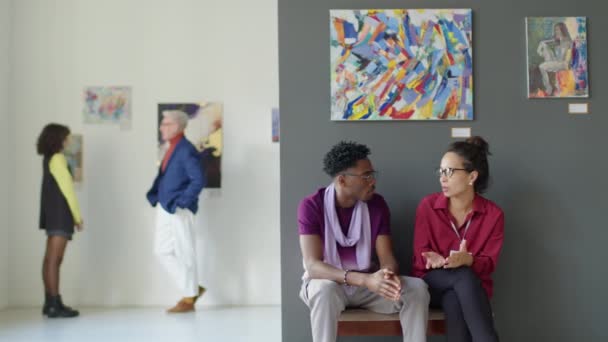 アートギャラリーとチャットの展示ホールに座っている若い多民族カップルの中長いショット — ストック動画