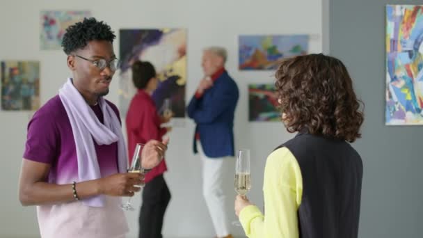 アフリカ系アメリカ人の男性がシャンパンを握り アートギャラリーで女性の友人との展覧会について話し合う中型ショット — ストック動画