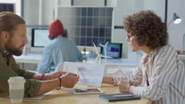 Erkek ve kadın yenilenebilir enerji geliştiricileri ofiste birlikte çalışırken kağıt üzerinde entrikaları tartışıyorlar.