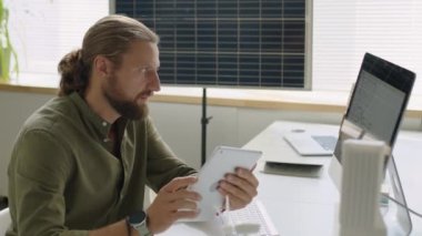 Dijital tablet kullanarak yenilenebilir enerji mühendisinin orta boy görüntüsü ve güneş panelleriyle çalışırken gülümsemesi.