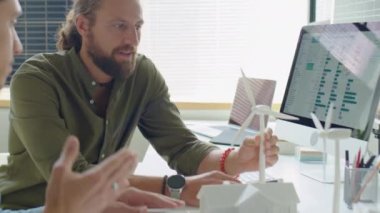 Ofisteki yenilenebilir enerji projesi üzerinde çalışırken, mühendisin iş arkadaşlarıyla konut ve rüzgar türbinlerinin modellerini tartışırken omuz üstü çekimleri.