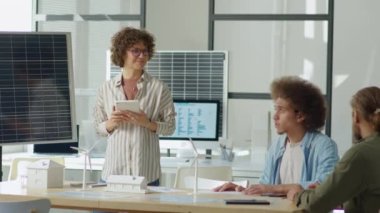 Kadın yenilenebilir enerji mühendisi dijital tablet tutuyor ve ofis toplantısında erkek yatırımcılara güneş enerjisi başlangıç projesiyle ilgili sunum yapıyor