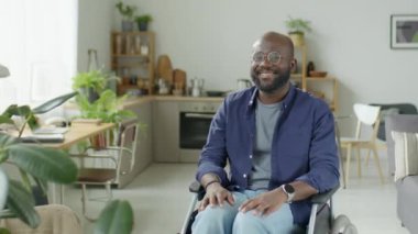 Özürlü, tekerlekli sandalyede oturan ve kameraya gülümseyerek poz veren mutlu Afrikalı Amerikalı adamın portresi.