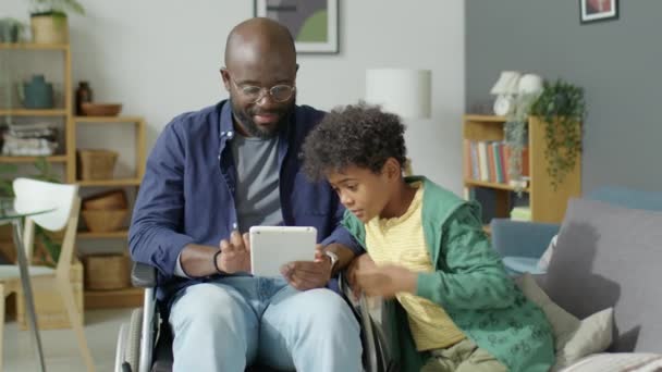 휠체어에 아프리카계 미국인 아버지와 아들이 집에서 디지털 태블릿에 재생의 — 비디오