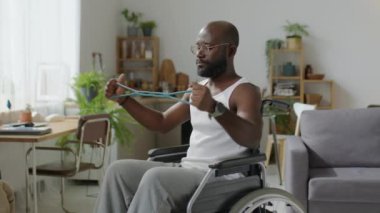 Tekerlekli sandalyede oturan ve antreman sırasında direniş bandıyla egzersiz yapan siyahi bir adam.