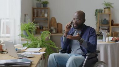Tekerlekli sandalyedeki Afrikalı Amerikalı evden uzakta çalışırken cep telefonuyla konuşuyor.