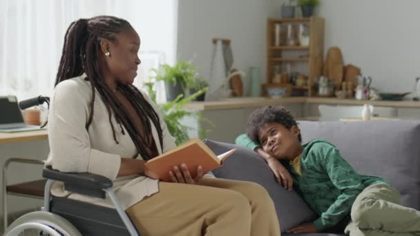 Älskar Afroamerikansk Mamma Rullstol Läser Bok Till Lille Son Som — Stockvideo