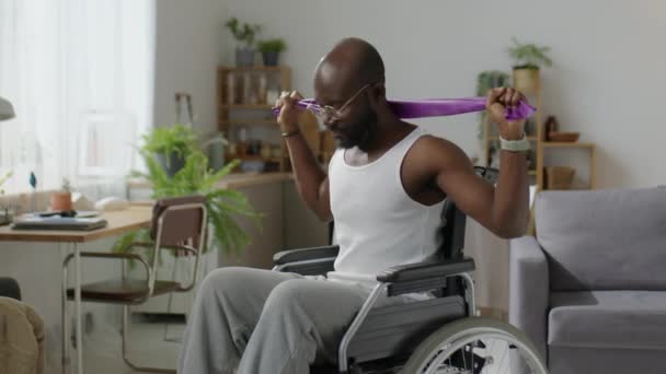 ホームワークアウト中にレジスタンスバンドで車椅子トレーニング中のアフリカ系アメリカ人の中型ショット — ストック動画