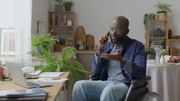 Афроамериканец Инвалидной Коляске Разговаривает Мобильному Телефону Работая Дистанционно Дома — стоковое видео