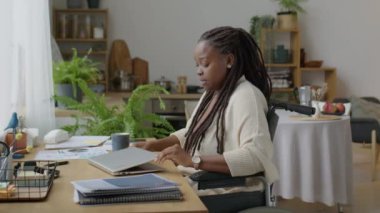 Tekerlekli sandalyede oturan genç Afrikalı Amerikalı kadın bilgisayarını açıp uzaktan yazıyormuş.