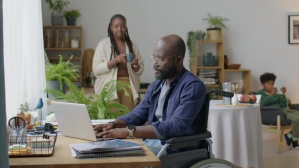 Homem Negro Cadeira Rodas Trabalhando Remotamente Laptop Casa Enquanto Esposa — Vídeo de Stock