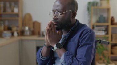 Engelli Afrikalı Amerikalı bir adamın tekerlekli sandalyede oturup avuç içleri kapalı dua edişini.