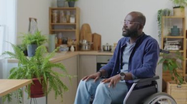 Özürlü, tekerlekli sandalyede oturan ve evde kameraya poz veren Afrikalı Amerikalı bir adamın portresi.