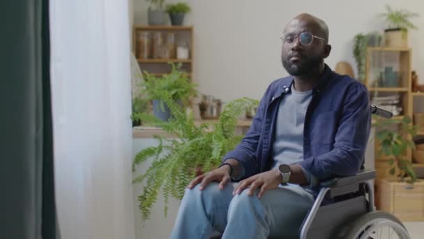 障害のあるアフリカ系アメリカ人の肖像画 車椅子に座って自宅の窓の横にカメラをポーズ — ストック動画